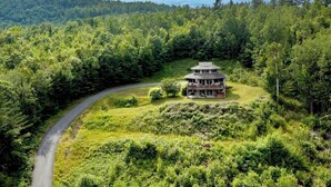 Un edificio de dos pisos con techo circular, rodeado de un bosque denso y un camino sinuoso.