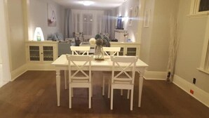A dining area with a white table and chairs, a vase with flowers, and a cabinet with glass doors. - Otylja Suite in Wortley Village (King Size Bed)
 (London)