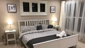 A bedroom with a bed, two bedside tables, a window with curtains, and framed pictures on the wall. - Otylja Suite in Wortley Village (King Size Bed)
 (London)