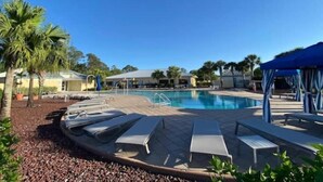 En swimmingpool med liggestole og parasoller, omgivet af palmer og bygninger.