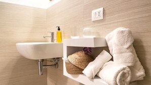 Un baño con un lavamanos blanco, un espejo y un estante con toallas y artículos de aseo.