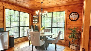 A wooden cabin interior with a dining area, large windows, a chandelier, and a sign indicating a coffee station. - Timber Nest | Stay Amongst the Trees (Blue Ridge)