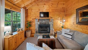 A cozy log cabin interior with a stone fireplace, wooden walls, a ceiling fan, and a comfortable seating area. - Timber Nest | Stay Amongst the Trees (Blue Ridge)