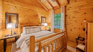 A wooden cabin bedroom with a bed, nightstands, a ceiling fan, and a window with curtains. - Timber Nest | Stay Amongst the Trees (Blue Ridge)