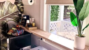 Una kitchenette compacta con ventana, una planta en maceta y un taburete pequeño.