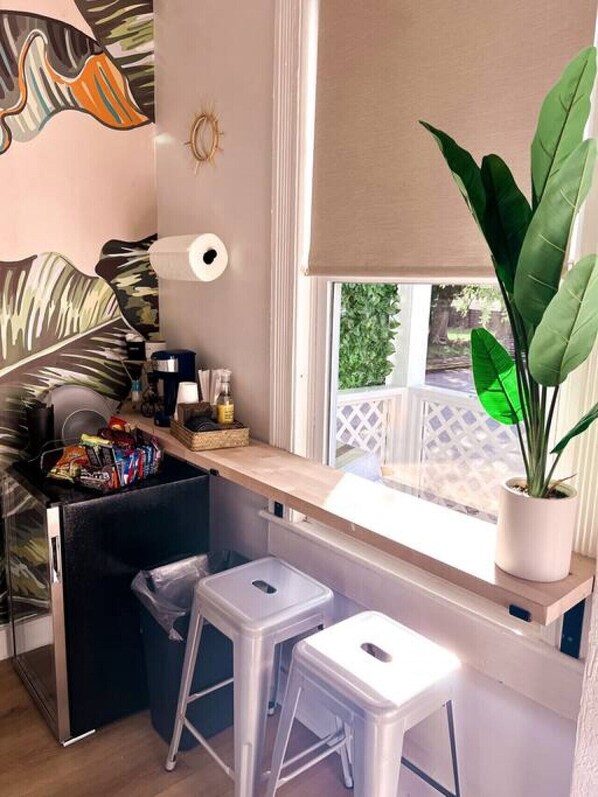 Una kitchenette compacta con ventana, una planta en maceta y un taburete pequeño.
