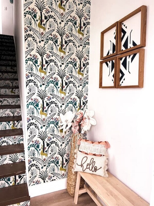 A staircase with a patterned wallpaper, a bench with a 'hello' pillow, and framed artwork on the wall.