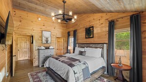 A wooden cabin bedroom with a bed, dresser, and a chandelier. - Mountain Bliss Chalet (Blue Ridge)