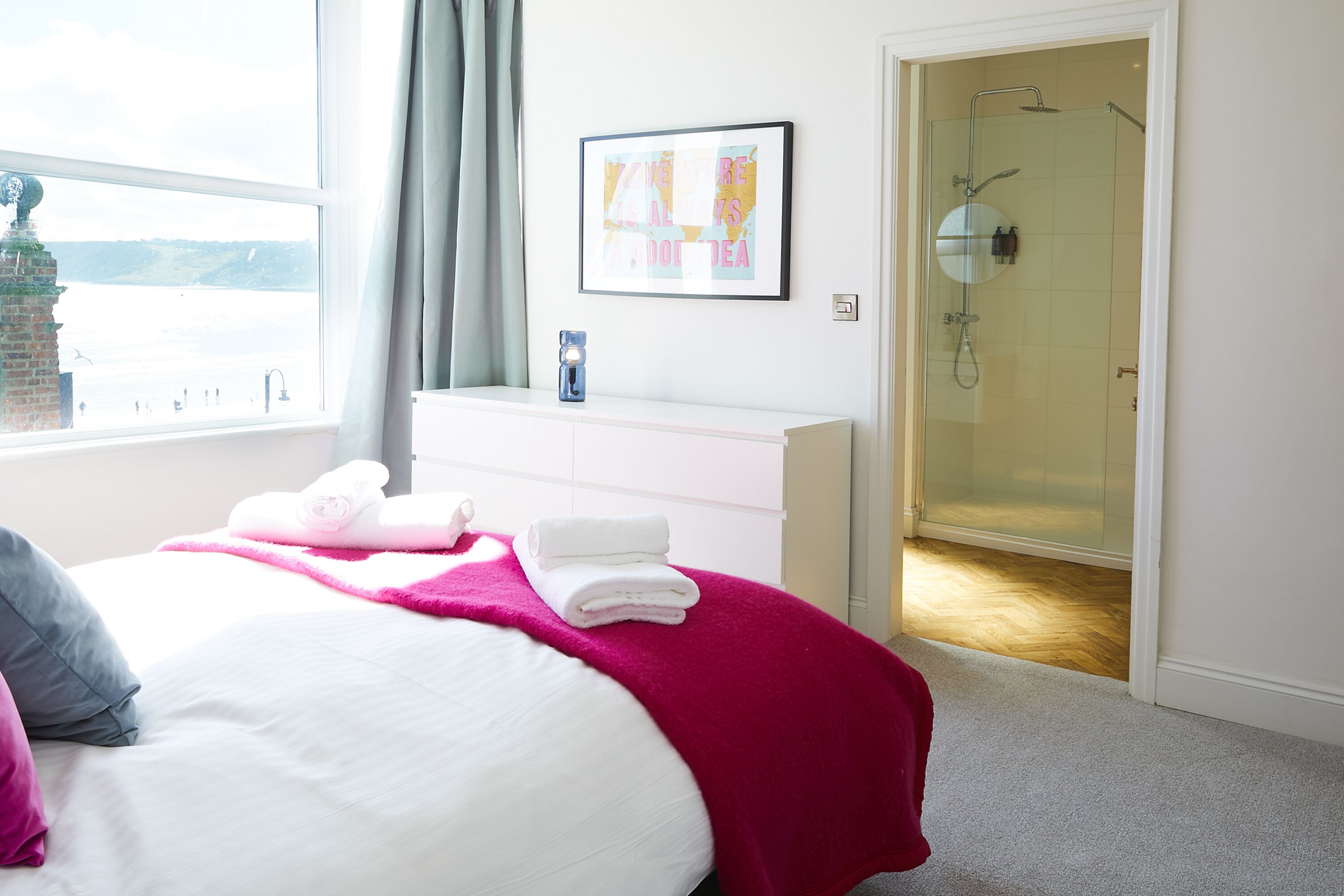 Ein Hotelzimmer mit Bett, einem weißen Schminktisch, einem gerahmten Bild und einer Duschkabine aus Glas.