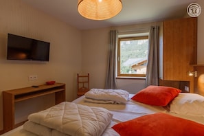 Une chambre avec deux lits, une télévision, un bureau et une fenêtre avec des rideaux.