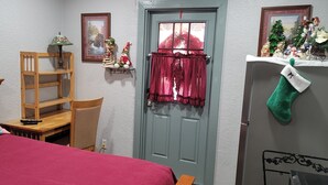 A bedroom with a bed, a wooden chair, a nightstand, a lamp, a shelf with Christmas decorations, a door with curtains, and a green stocking on the wall. - Farmhouse room 15minutes to, caverns state park
 Falling waters chipley Florida  (Cottondale)