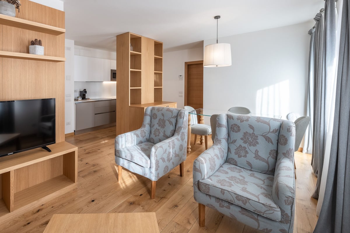 A modern living room with a TV, two patterned armchairs, a wooden coffee table, and a built-in bookshelf.