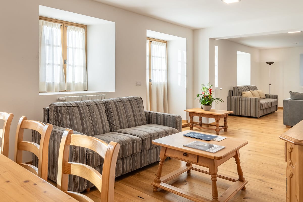 A modern living room with a sofa, wooden chairs, a coffee table, and a small table with a plant.