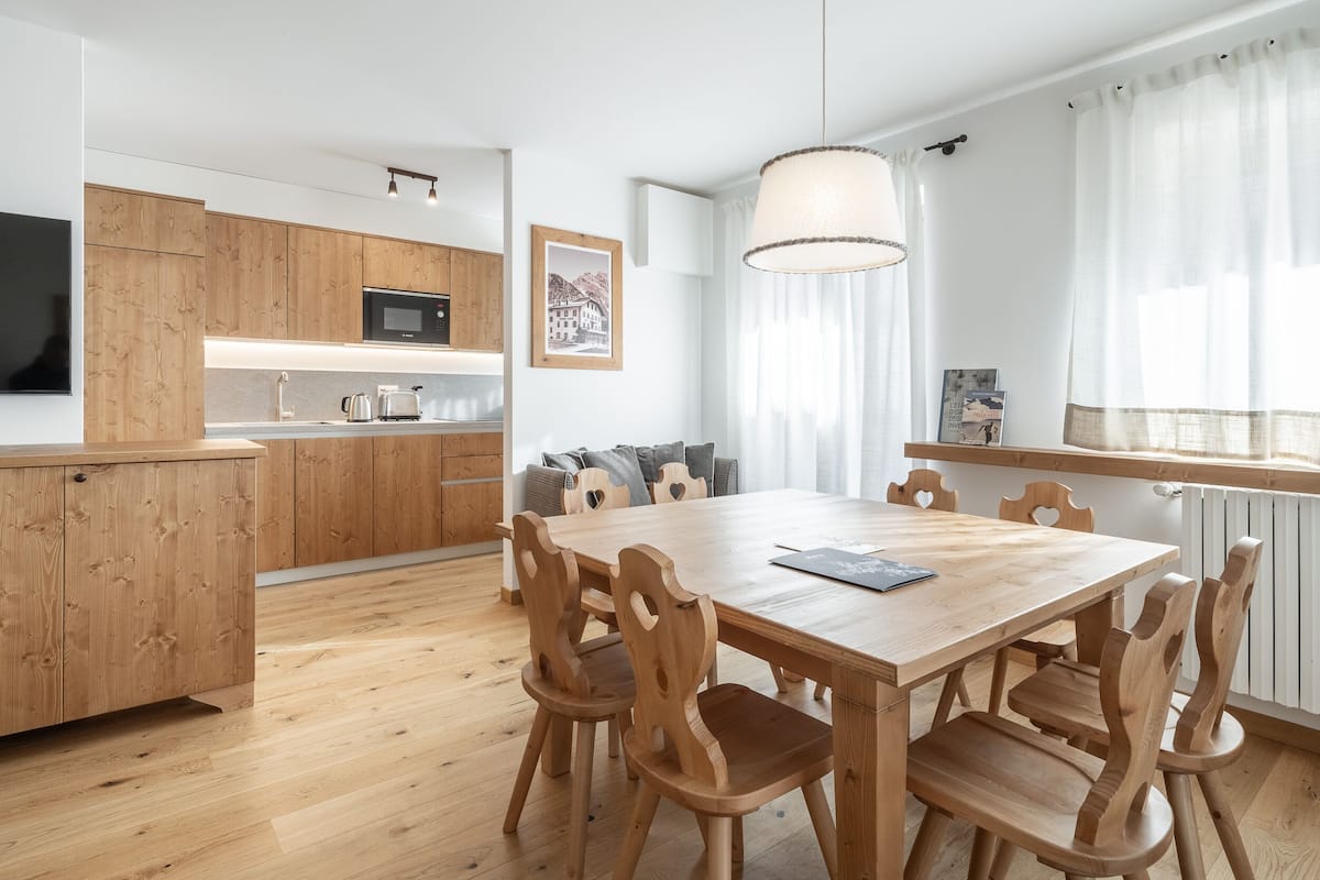 A modern kitchen with wooden cabinets, a microwave, and a dining area with a wooden table and chairs.