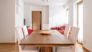Zona pranzo con tavolo in legno, sedie bianche e divano rosso.