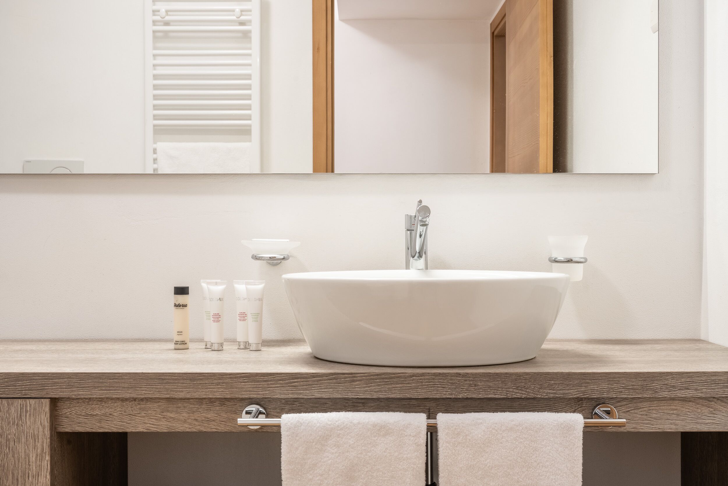 Un baño moderno con un lavamanos blanco, dos toalleros y un espejo sobre el lavamanos.