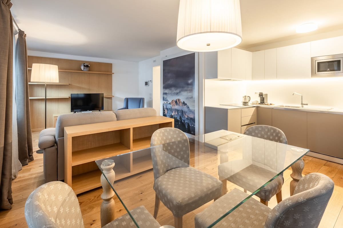 A modern living room with a sofa, TV, and glass dining table with chairs.