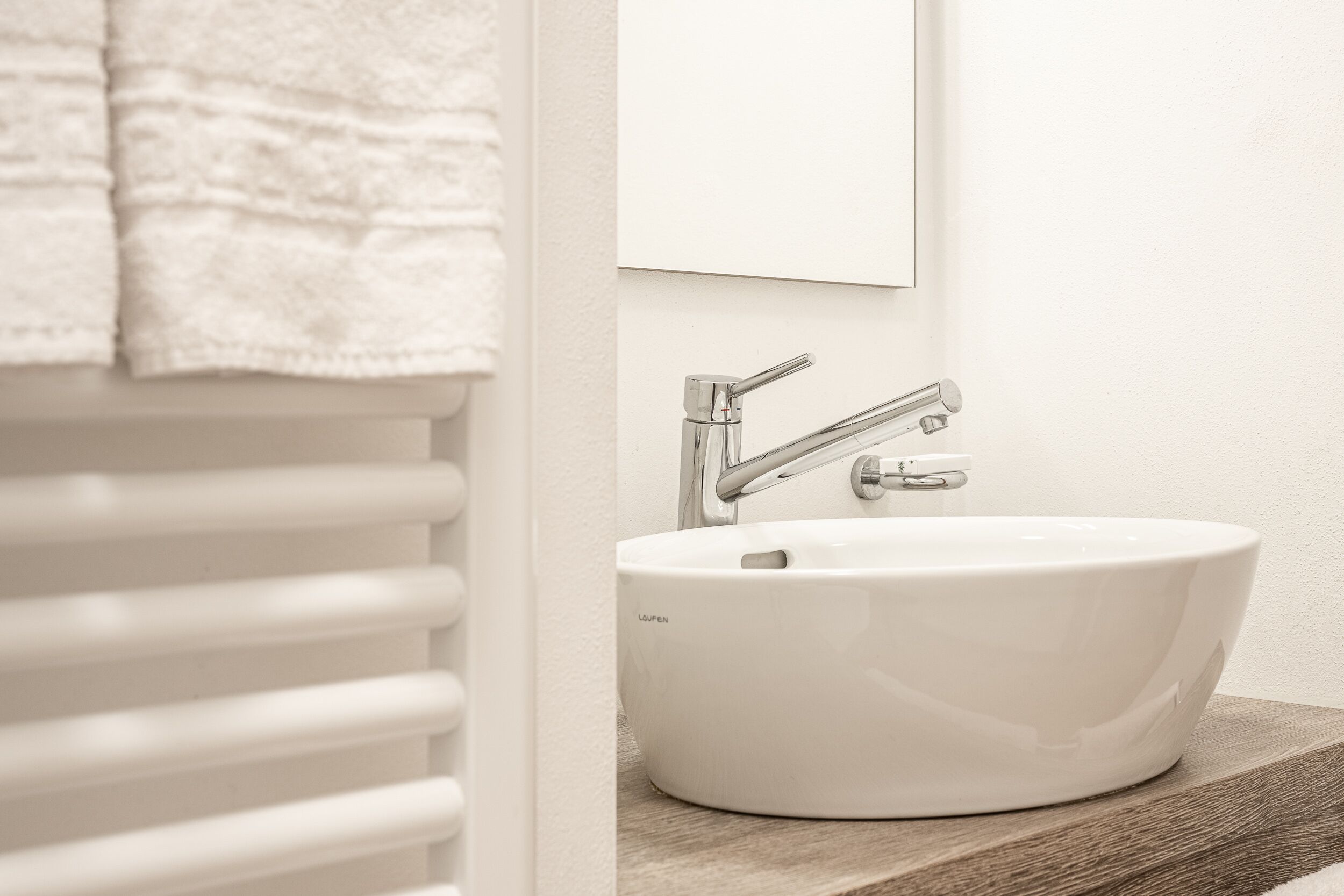A bathroom with a white sink, chrome faucet, and a towel hanging on a white radiator.