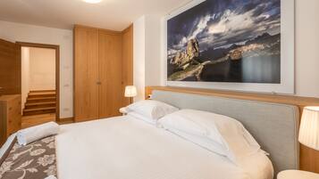 A hotel room with a bed, a nightstand, a lamp, a wooden wardrobe, and a framed landscape painting.