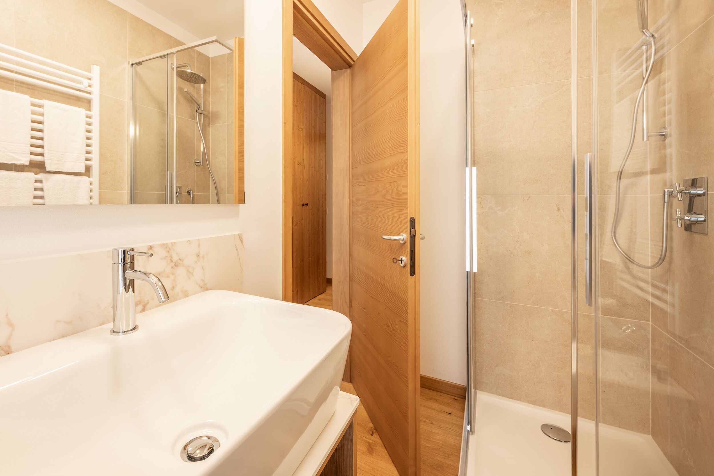 Un baño moderno con un lavamanos grande de color blanco, una ducha con cerramiento de vidrio y una puerta de madera.
