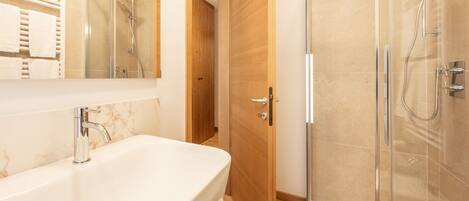 Un baño moderno con un lavamanos grande de color blanco, una ducha con cerramiento de vidrio y una puerta de madera.