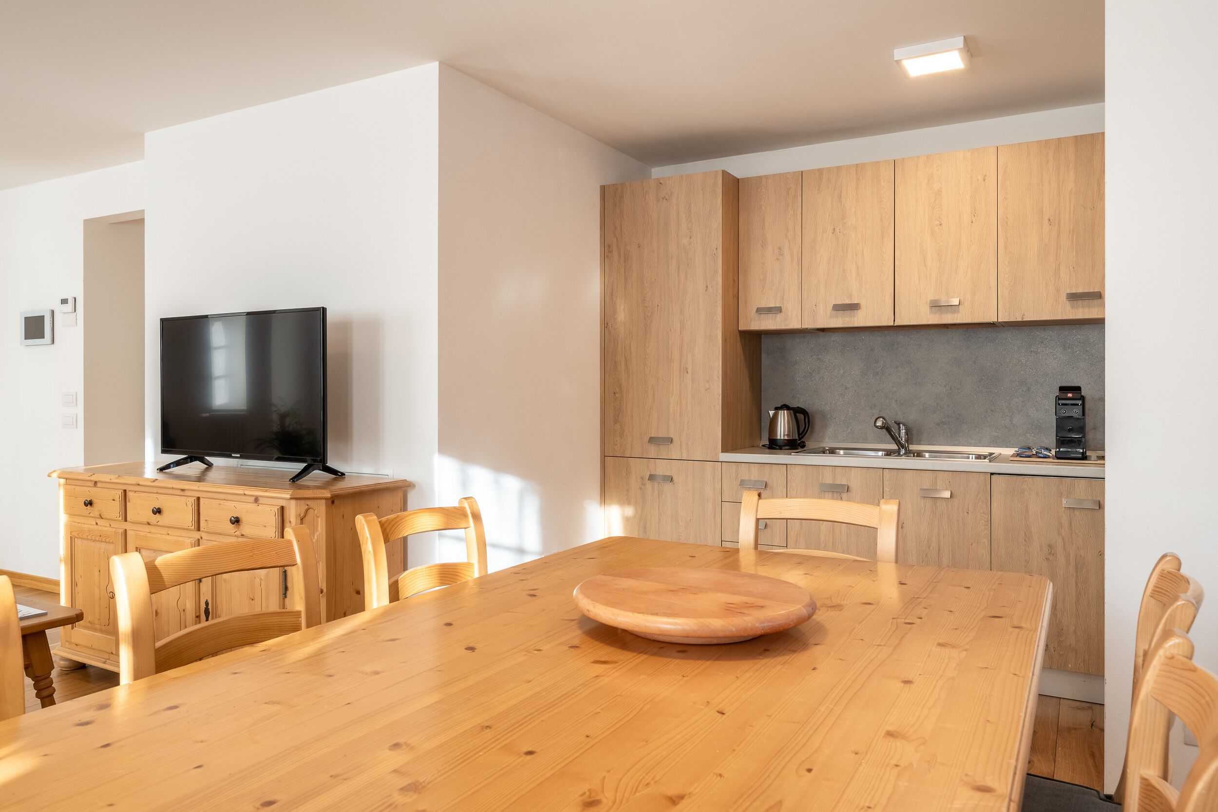 A modern kitchen with wooden cabinets, a built-in oven, and a coffee machine.