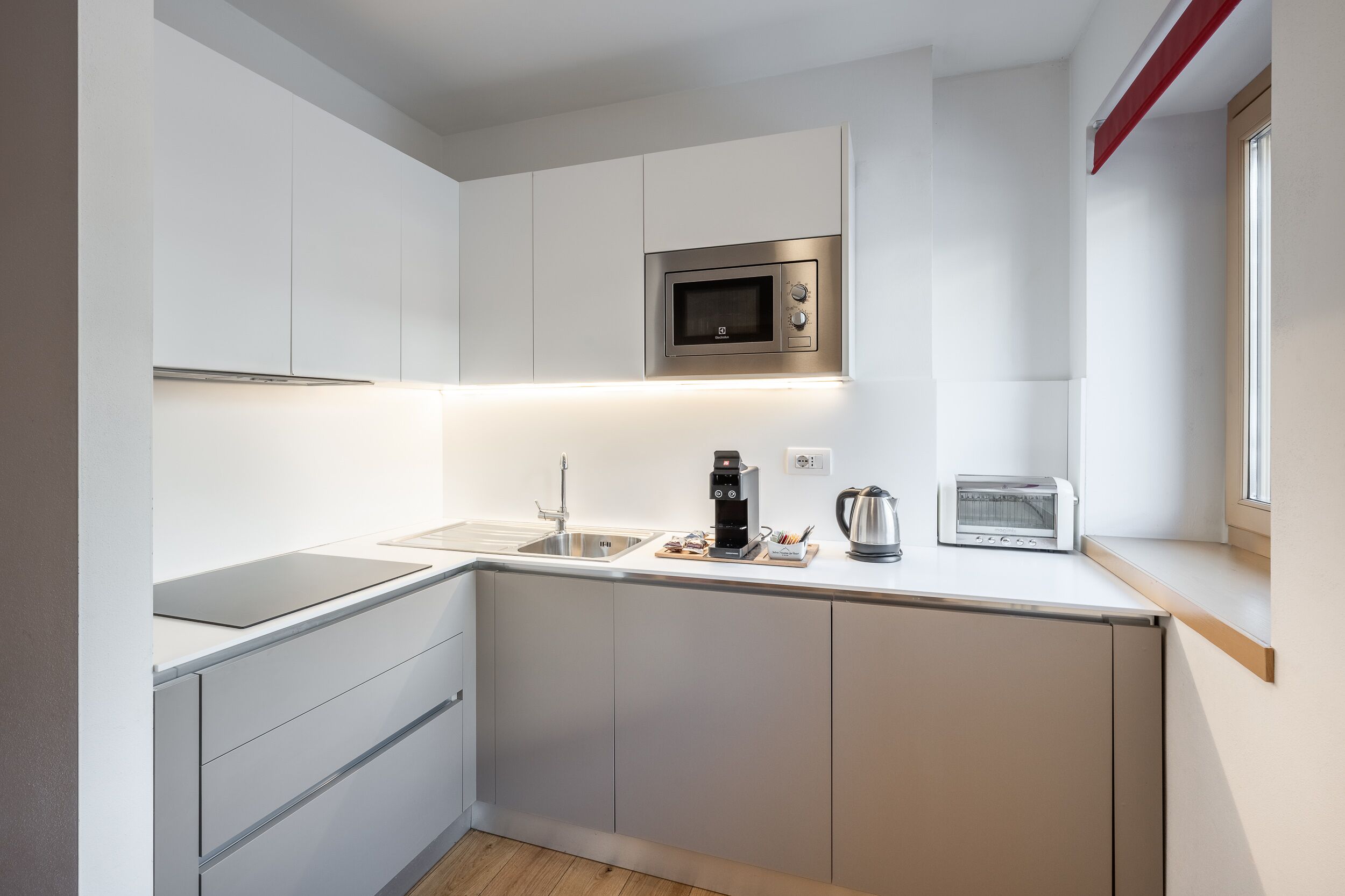A modern kitchen with white cabinets, a stainless steel microwave, a coffee maker, and a toaster.