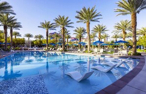 A pool area with palm trees, lounge chairs, and umbrellas.
