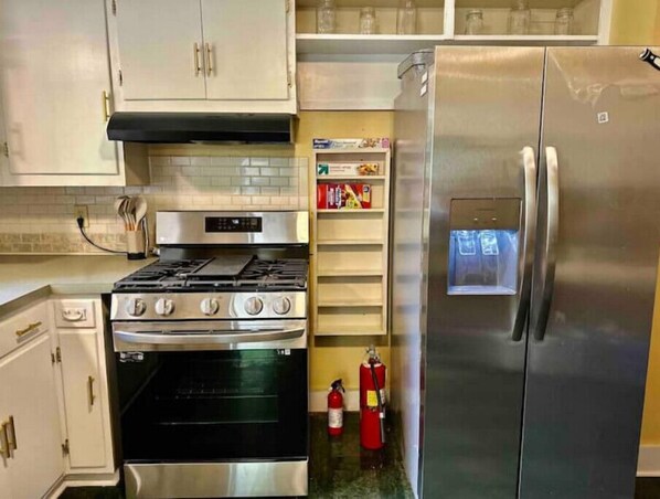Kitchen area with a refrigerator, oven, and gas stove, along with a shelf unit and gold-handled cabinets.