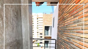 A narrow corridor with a concrete wall on one side and a brick wall on the other, leading to a balcony with a metal railing.