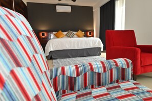 Ein Hotelzimmer mit einem Bett, einem roten Sessel und einem gestreiften Sofa.