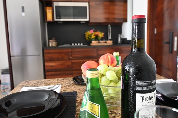 A kitchen counter with a bottle of Protos, a bowl of grapes, and a microwave in the background.