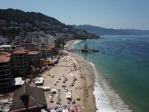 Uma praia com guarda-sóis, um cais e edifícios ao fundo.