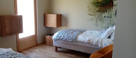 A bedroom with a bed, a chair, a wooden cabinet, and a wall-mounted TV.