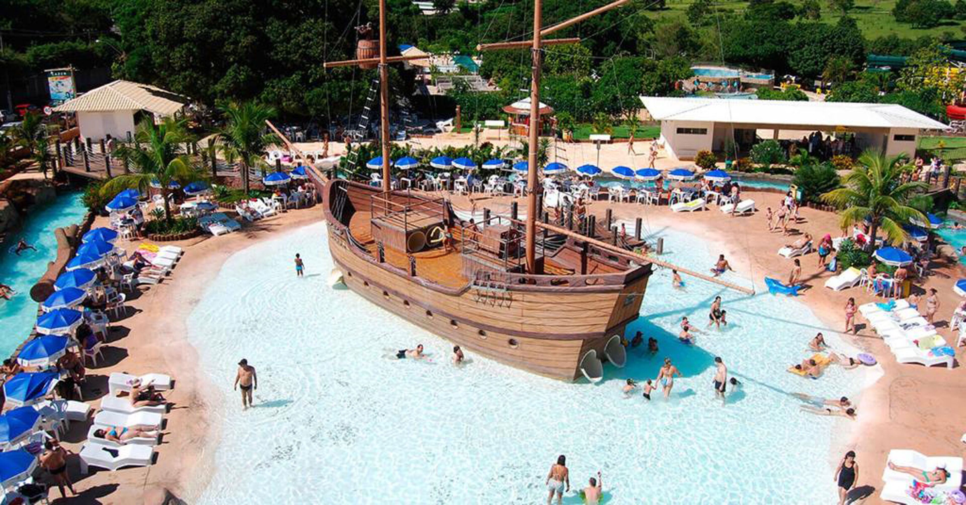 A beach with a wooden ship-shaped pool surrounded by lounge chairs and umbrellas.