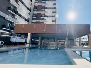 En modern byggnad med en swimmingpool, utomhusplats och en överbyggd entré.
