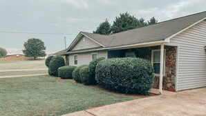 A single-story house with a stone foundation, a covered porch, and a well-maintained lawn. - Cozy Cedartown Retreat
 (Cedartown)