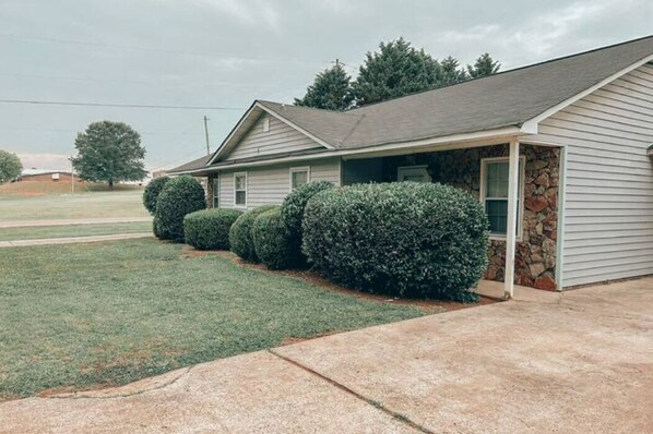 Een gelijkvloers huis met een stenen fundering, een overdekte veranda en een verzorgd gazon.