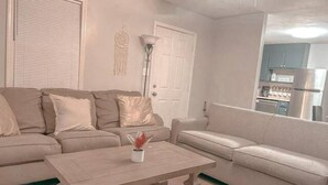 A living room with a beige sofa, a wooden coffee table, and a door with a white wall decoration. - Cozy Cedartown Retreat
 (Cedartown)