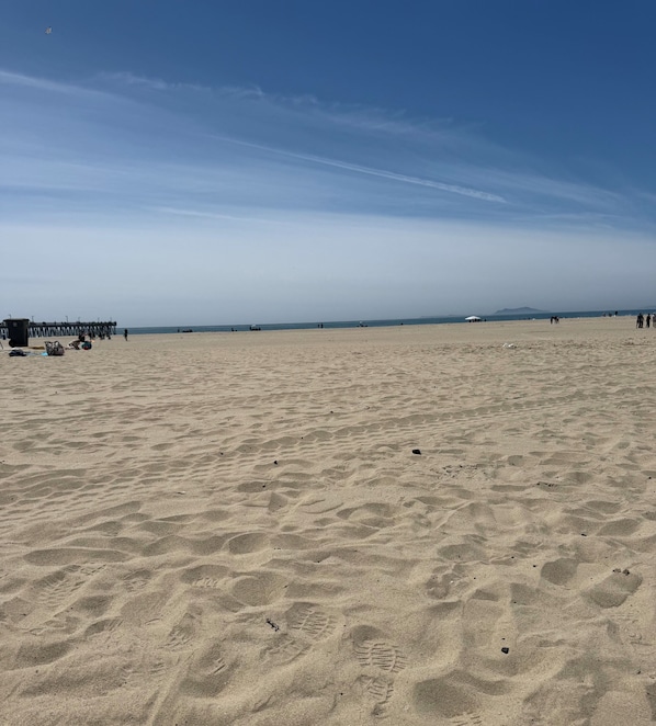 A wide sandy beach with footprints, a pier, and a clear sky.