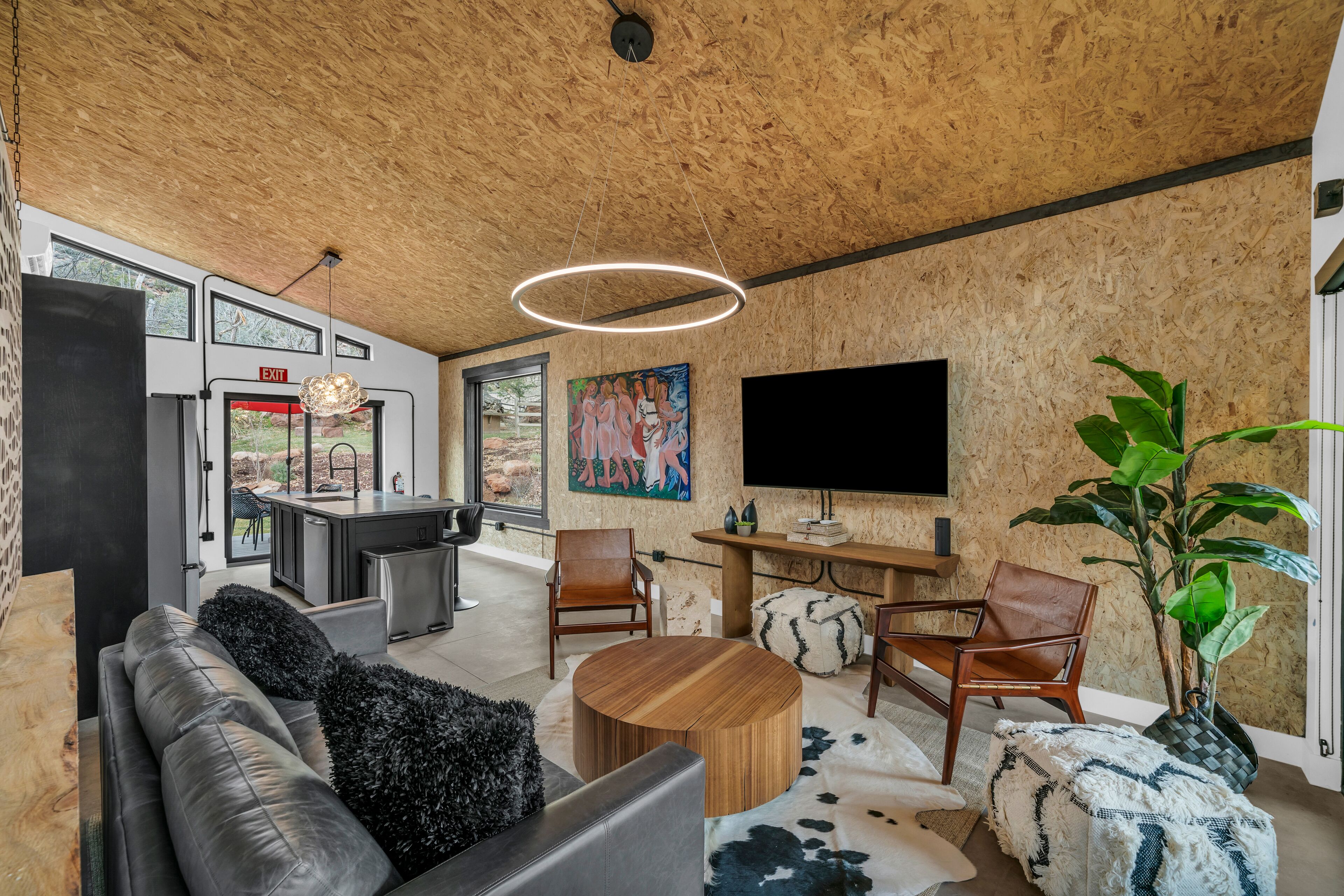 Ein modernes Wohnzimmer mit Holzboden, einem großen Fernseher, einer Couch, Sesseln, einem Couchtisch und einem Bild an der Wand.
