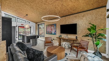 Una sala de estar moderna con techo de madera, televisor grande, sofá, sillas, mesa de centro y un cuadro en la pared.