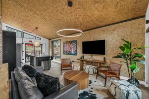 Una sala de estar moderna con techo de madera, televisor grande, sofá, sillas, mesa de centro y un cuadro en la pared.