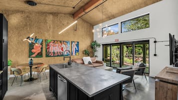Une cuisine moderne dotée d’un îlot central, d’un coin repas avec des chaises et d’une grande fenêtre donnant sur un espace verdoyant.