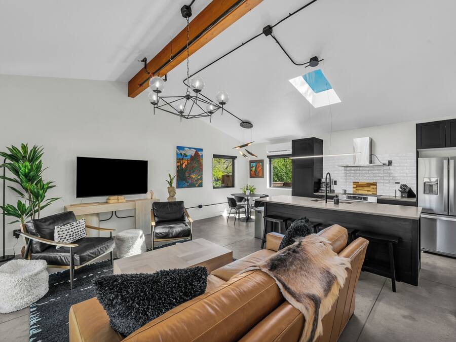 Un salon moderne doté d’un grand téléviseur à écran plat, de canapés en cuir et d’un coin repas avec une cuisine en arrière-plan.