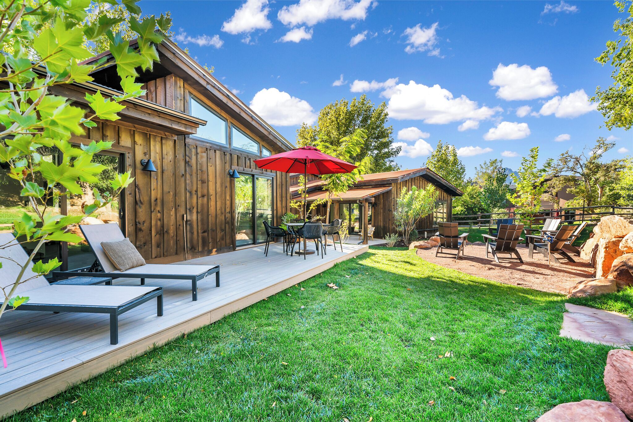 Una cabaña de madera con terraza, mobiliario exterior y césped cuidado.