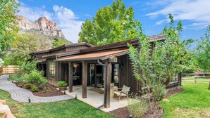 Una casa moderna con un patio, mobiliario exterior y un paisaje de montañas al fondo.