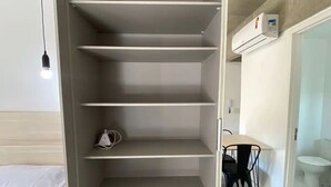 A room with a bed, a desk, a chair, and a wardrobe with multiple shelves. - Novo Studio Prox. Av Paulista, Garagem e Academia (Consolação São Paulo)