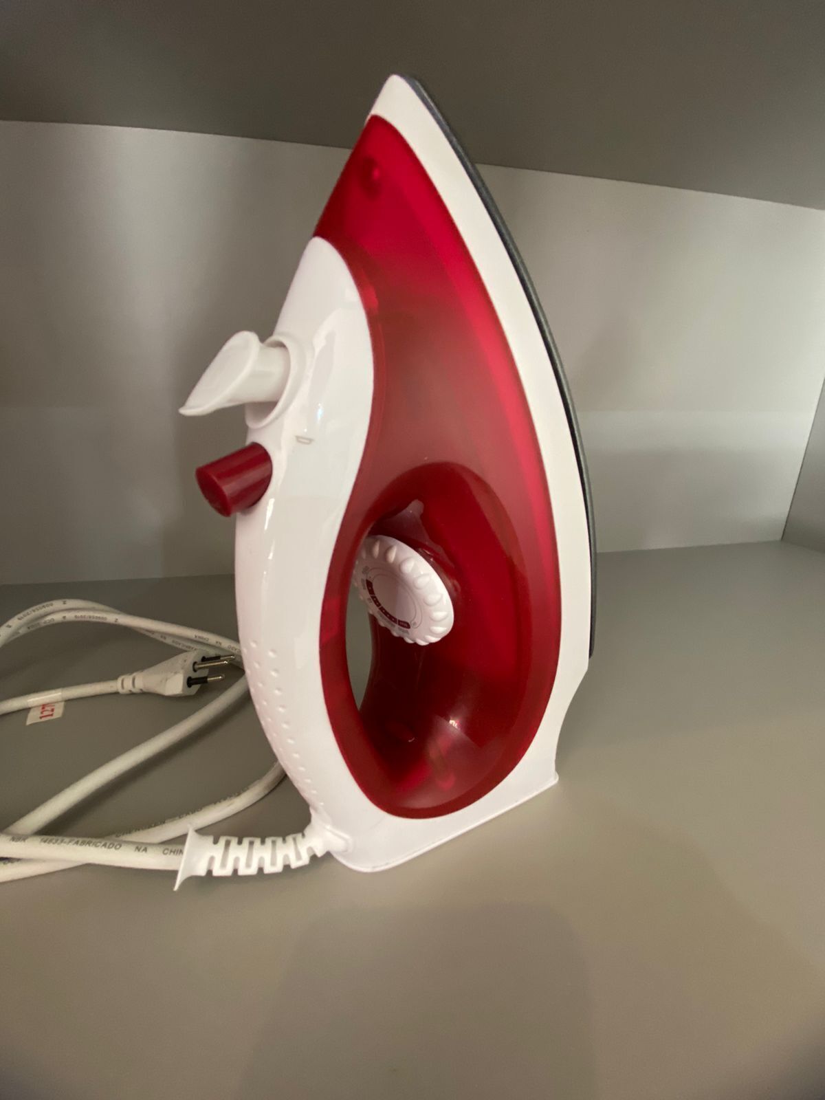 A red and white iron with a cord plugged in.