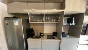 A compact kitchen with a built-in refrigerator, a sink, and a microwave. - Novo Studio Prox. Av Paulista, Garagem e Academia (Consolação São Paulo)